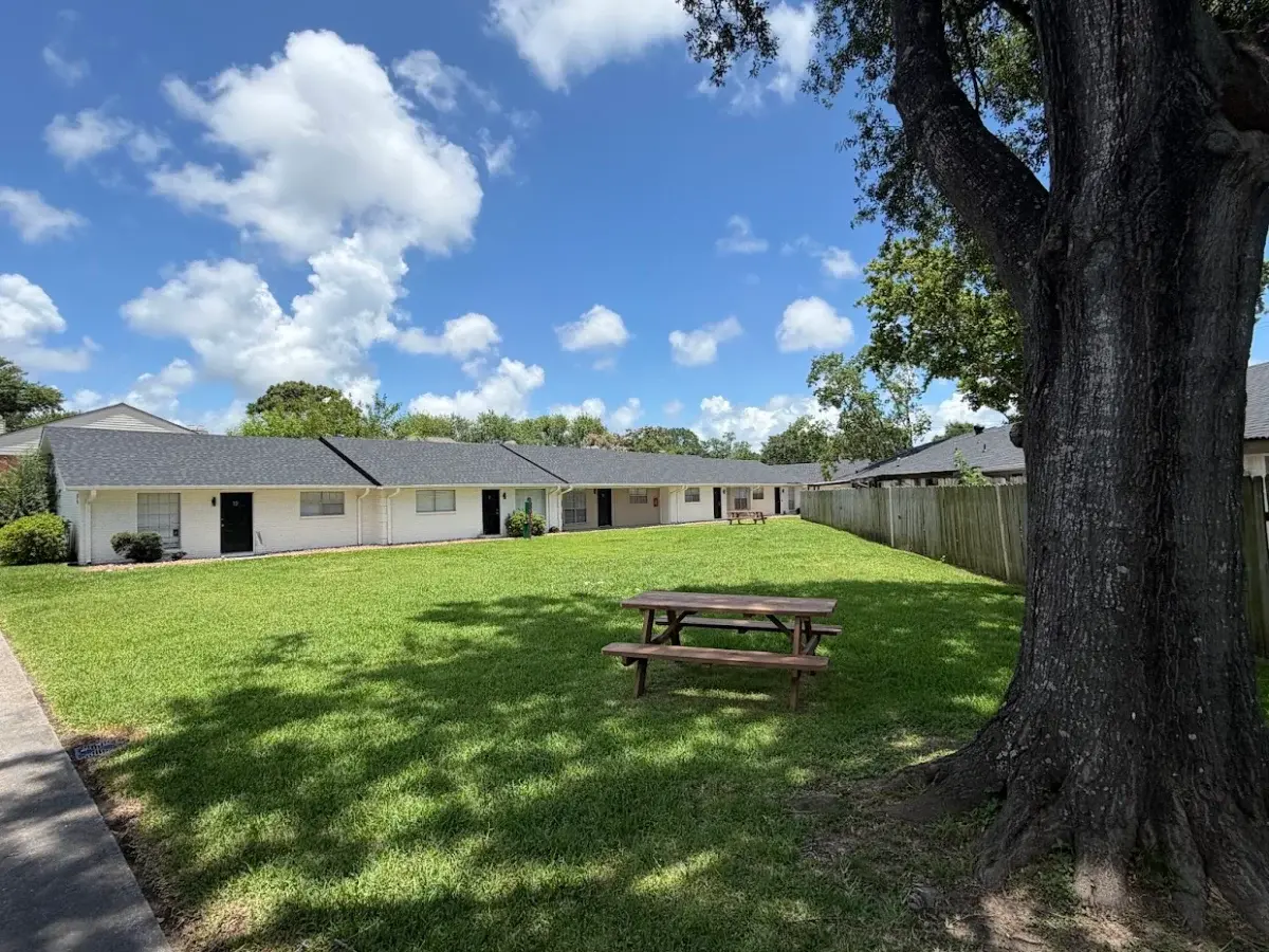 Luna Bay Townhomes courtyard: a mown lawn with a picnic table under a mature oak, single-storey white brick townhomes behind.
