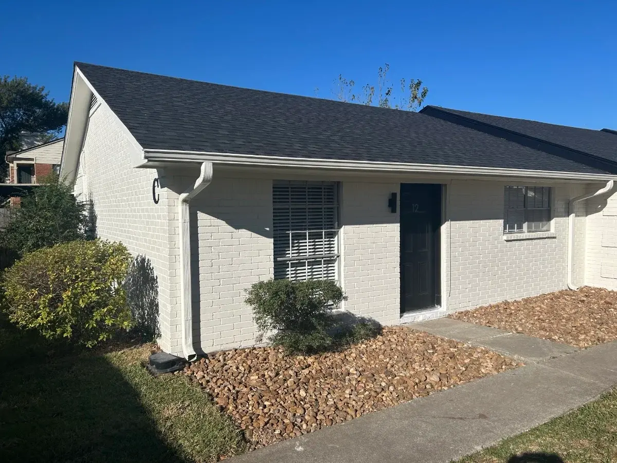Exterior of a renovated Luna Bay townhome unit: painted white brick, new dark roof, and gravel bed along the entry walk.