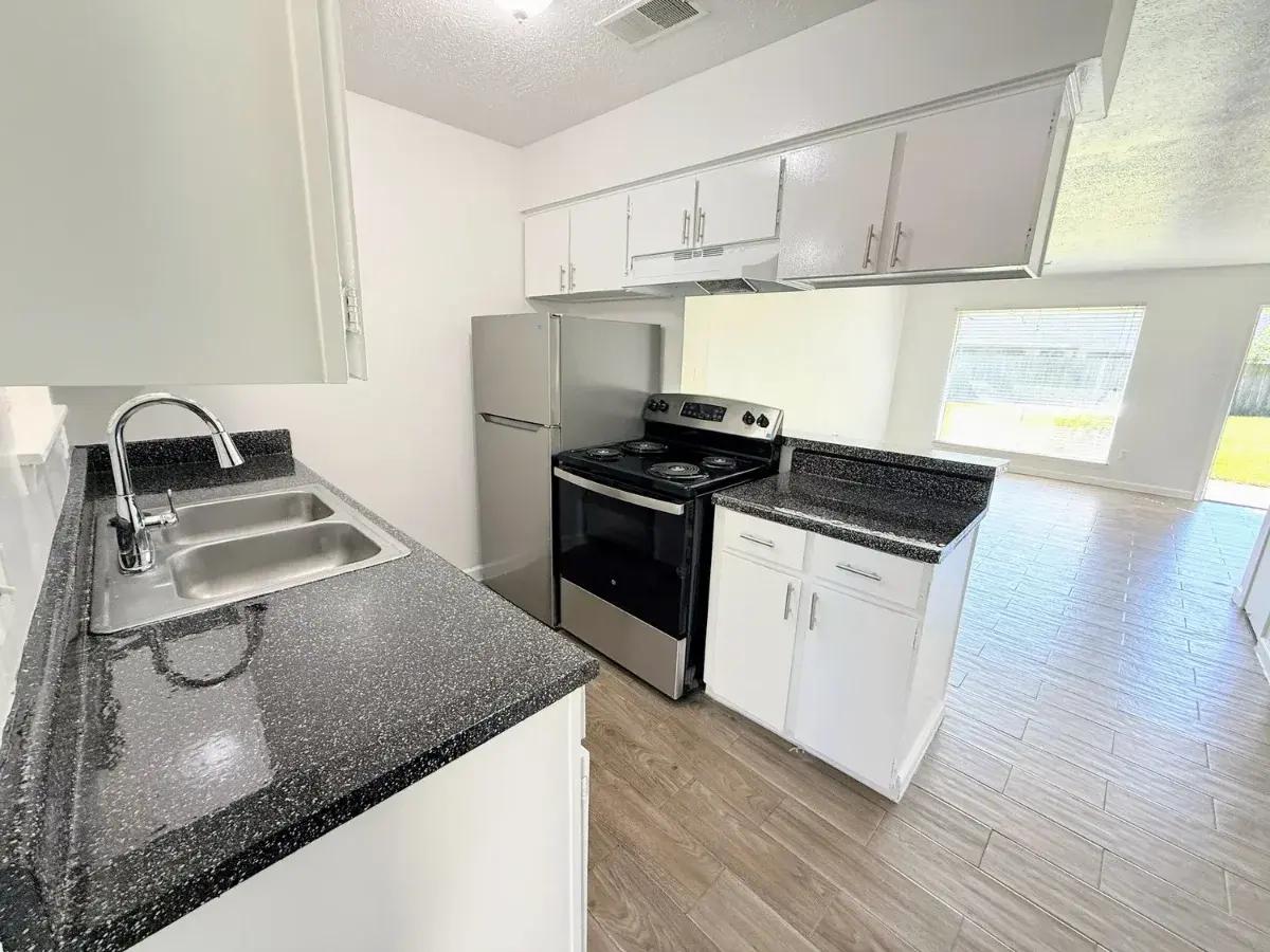 Renovated Luna Bay unit interior: kitchen with stainless appliances, stone-look counters, and wood-look flooring opening to the living area.